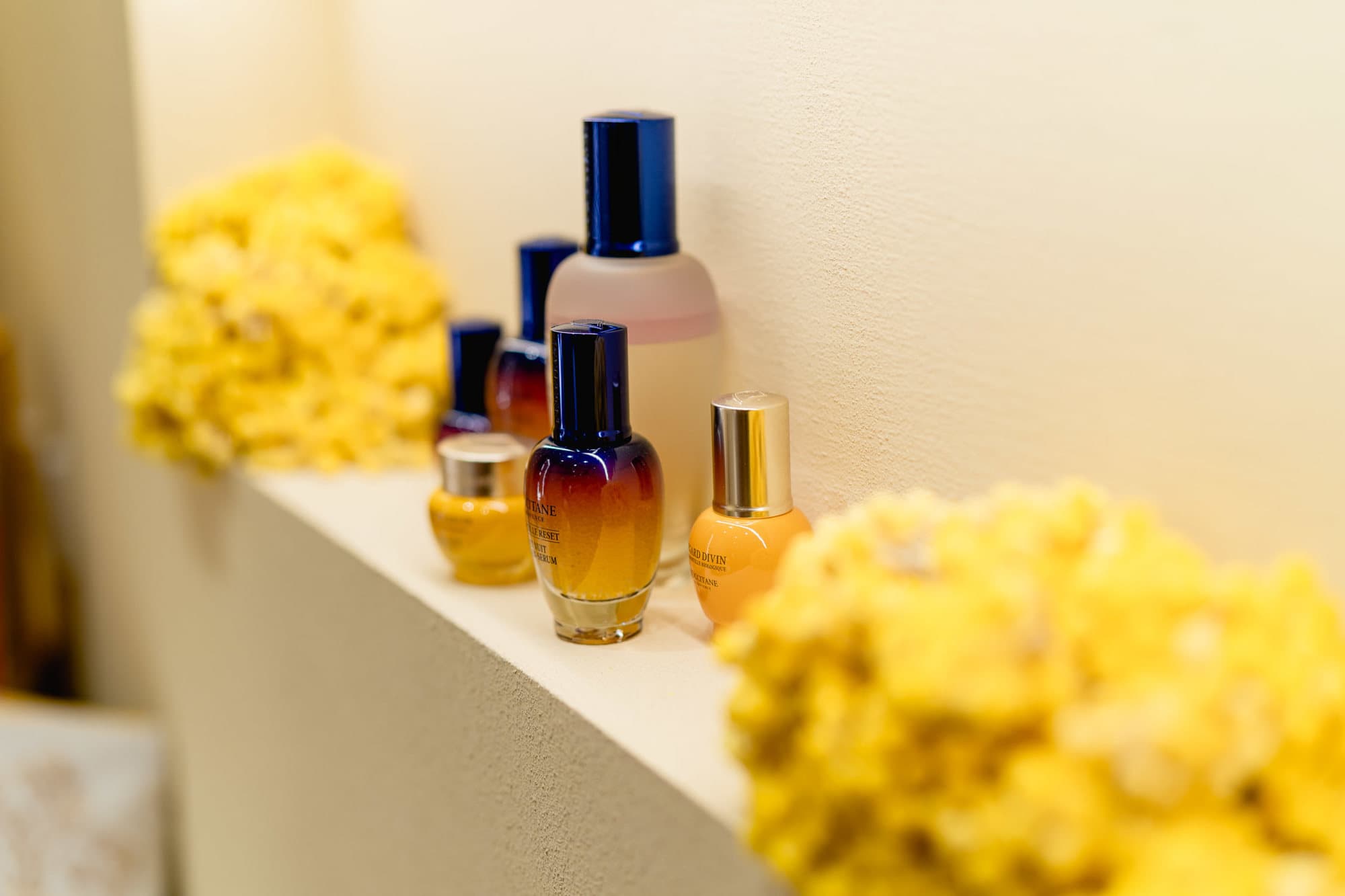 L'Occitane Immortelle skincare serums and oils lined along a cream ledge between two natural yellow sea sponges.